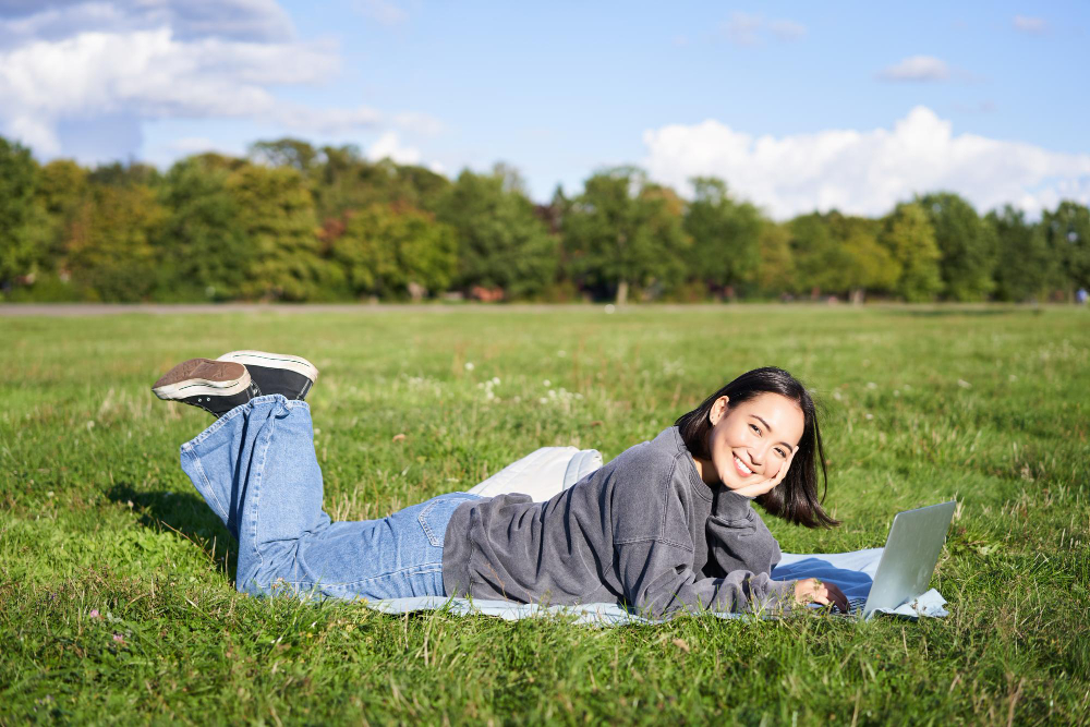 Leisure and people happy young woman lying in park on blanket using laptop relaxing outdoors